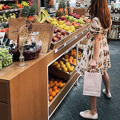 A person wearing a pair of Keds Champion Originals in white, standing in front of a fruit stand.